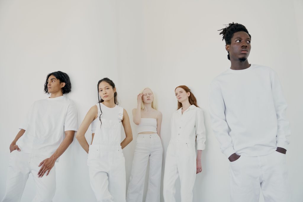 Five models wearing monochrome all-white outfits standing together in a minimalist studio setup.