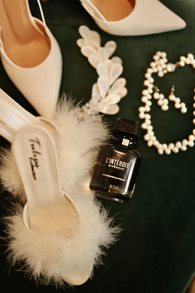 White heels with pearl jewelry, accessories, and perfume bottle on green background